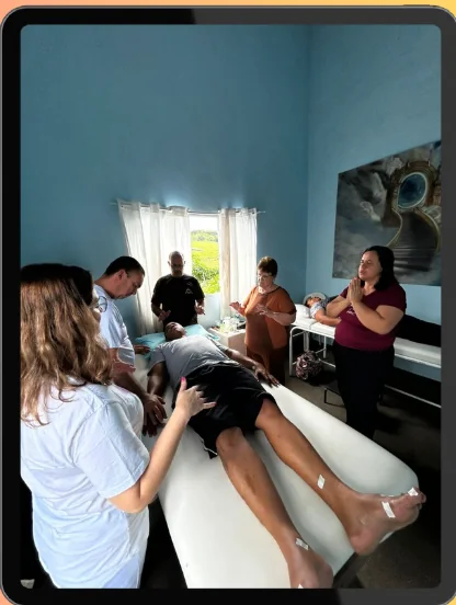 Atendimento espiritual presencial em sala com maca e equipe ao redor